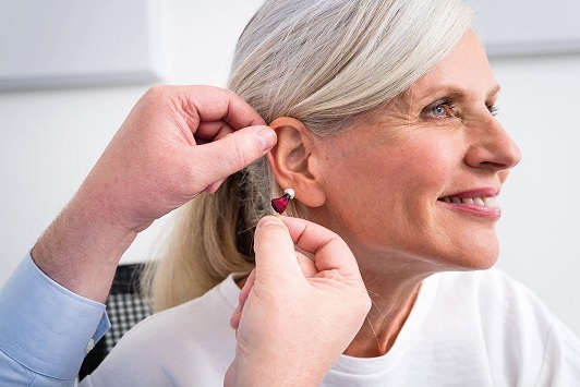 Ältere Frau bekommt ein modernes Hörgerät ins Ohr eingesetzt und lächelt freundlich.